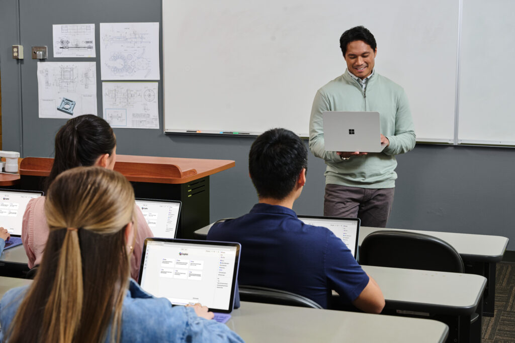 A teacher holding a laptop leading a classroom in front of pupil also looking at laptops.