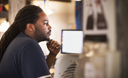 Image of a tech worker stroking his beard and looking at a computer monitor.