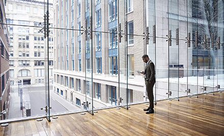 Image of a worker checking his phone while looking out a window over a cityscape.