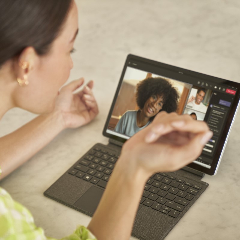 Hybrid employee sitting in kitchen working on 2-in-1 tablet in laptop mode on Teams call.