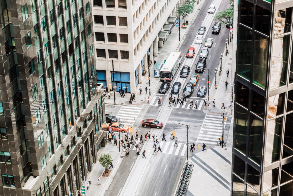 A view of a city intersection from above with people in crosswalks and cars driving on the roads.