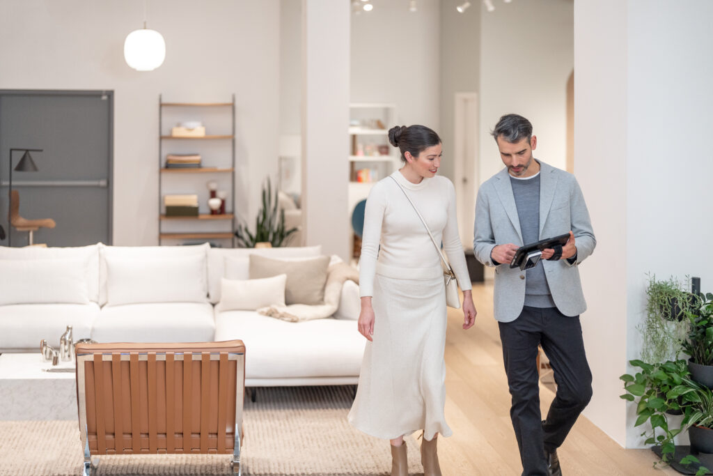 Man holding a tablet walking with a woman through a living room showroom