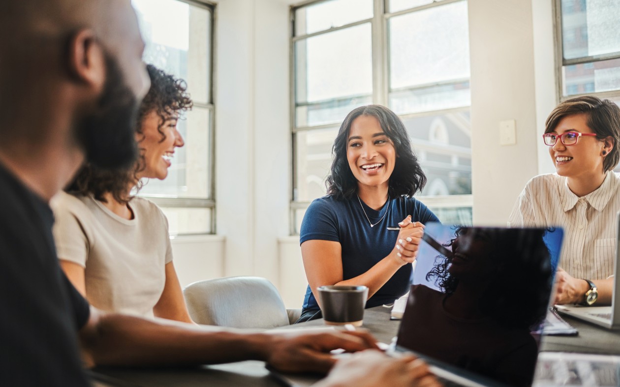 A diverse group of coworkers collaborate in an office space while one takes notes on his laptop.