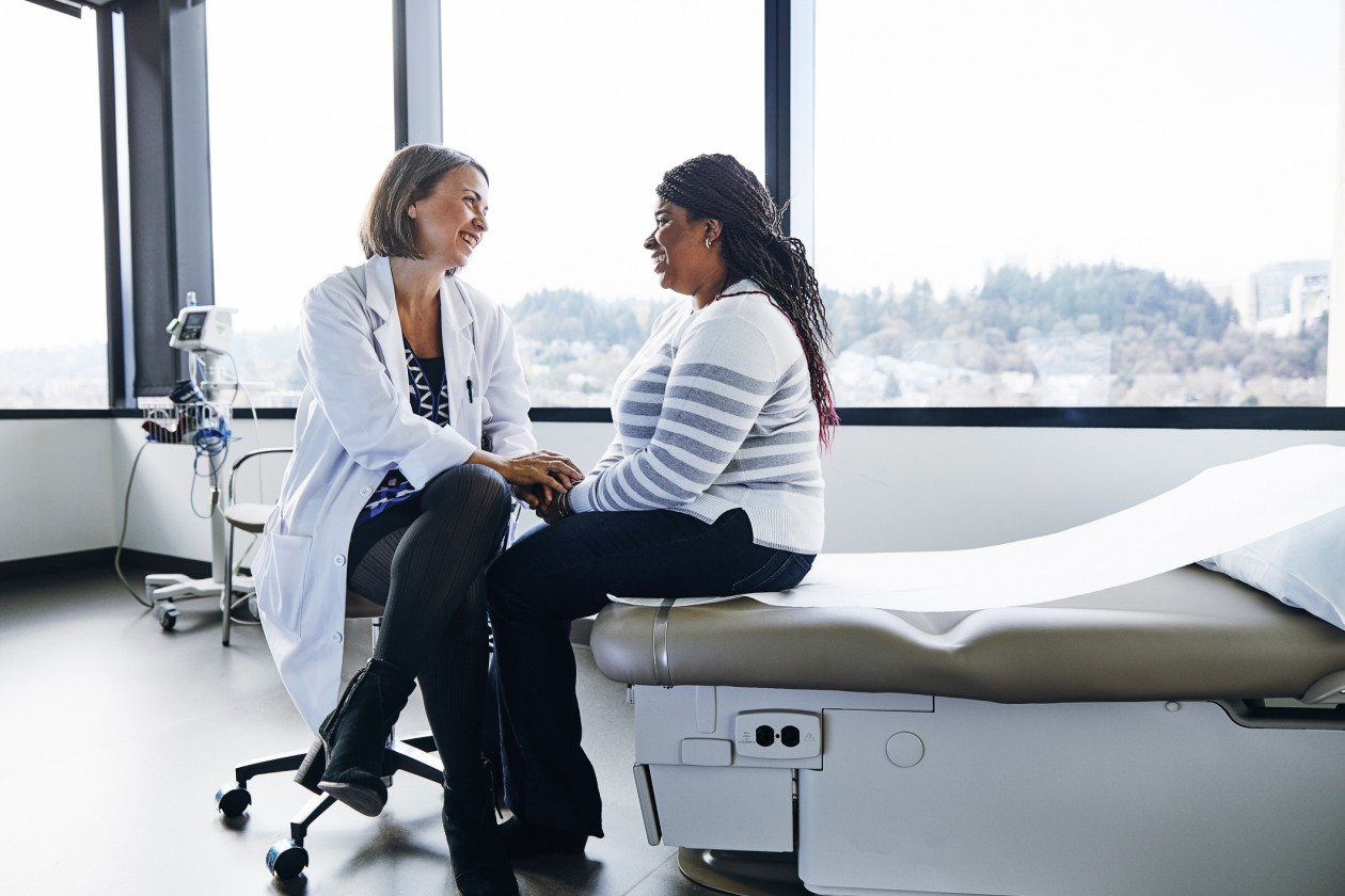 A smiling doctor talks with a woman in a hospital room.