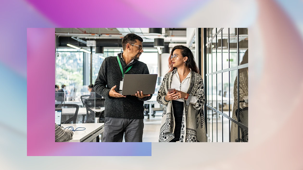 A man and a woman walking through an office hallway having a conversation.