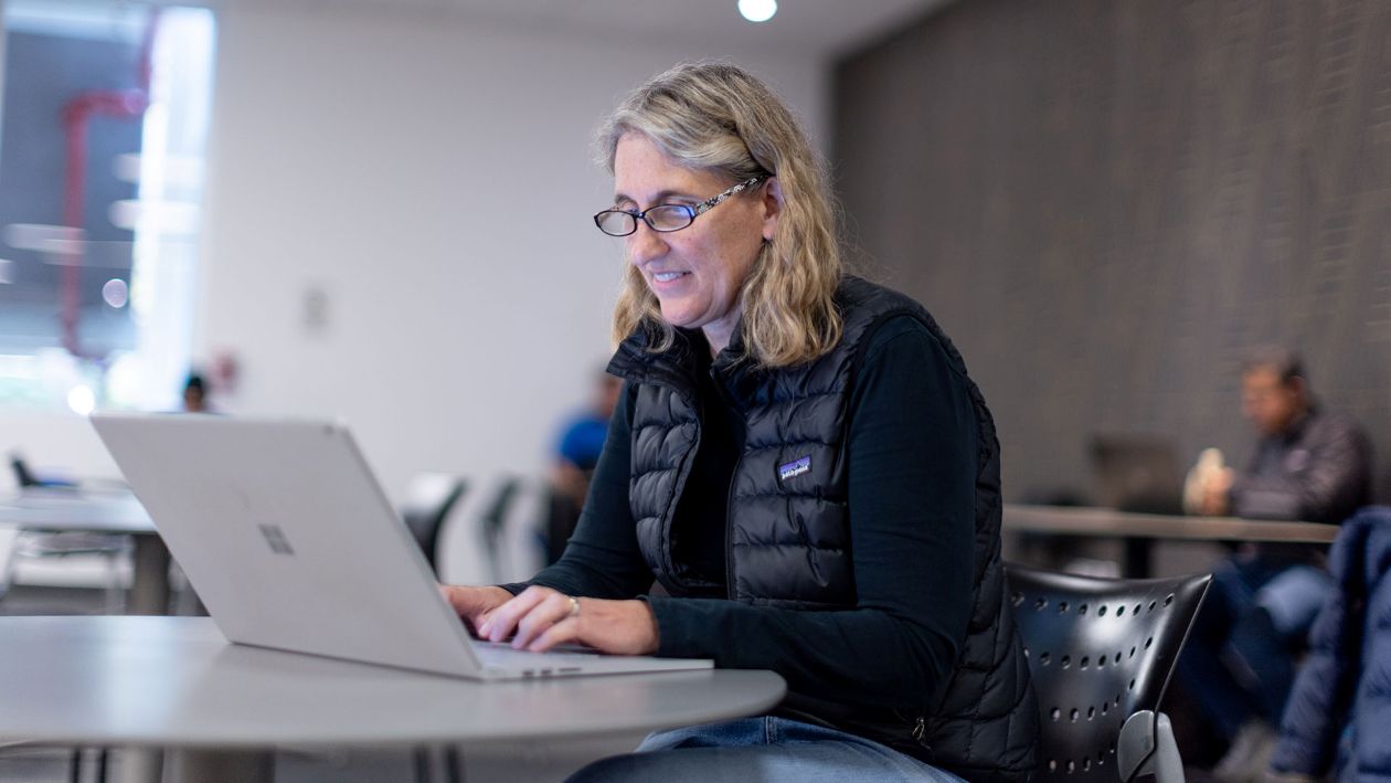 Woman in black vest and shirt typing on a laptop in a cafe.