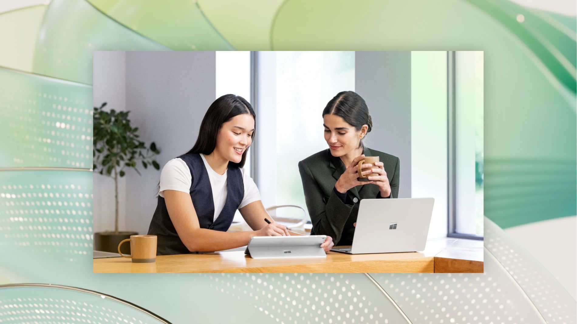 Two professionals collaborate at a desk using a Microsoft Surface laptop and tablet, reviewing digital information together in a modern office setting.