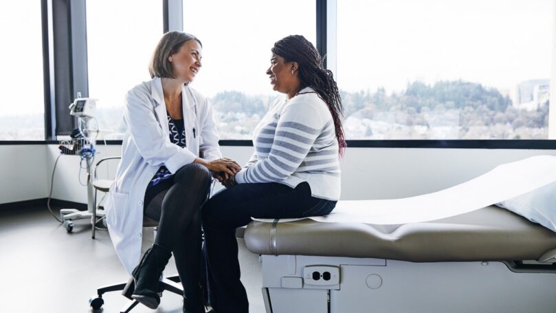 A smiling doctor talks with a woman in a hospital room.