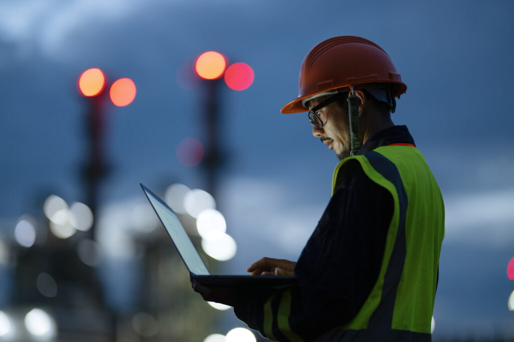 Boosting Key Front-line Operations Through Digitization to Driving Sustainability in Oil and Gas Industry. Side view of Engineer working over a laptop computer to analyze insights related to the production of energy in field operation.