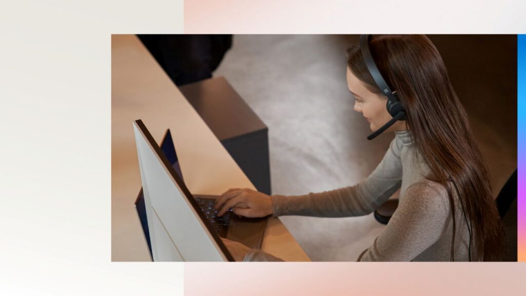 A person working on a computer while wearing a headset with a mouthpiece.