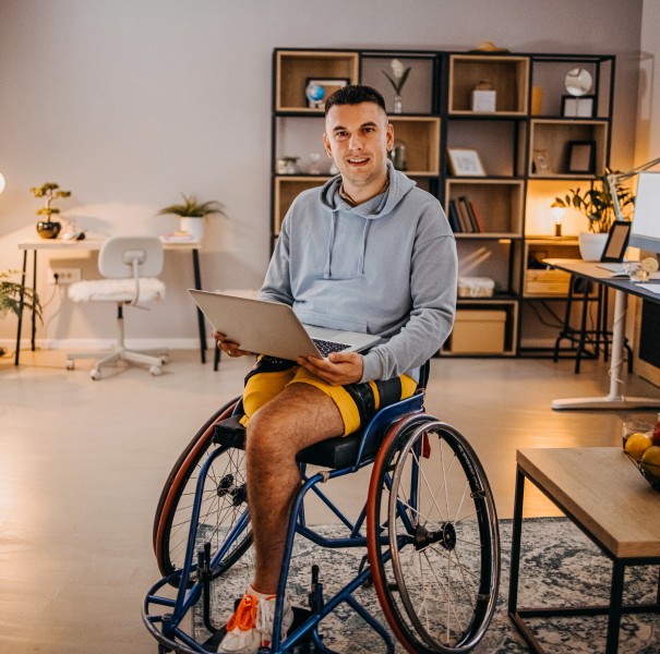 Portrait of a man in a wheelchair holding a laptop in his home office.
