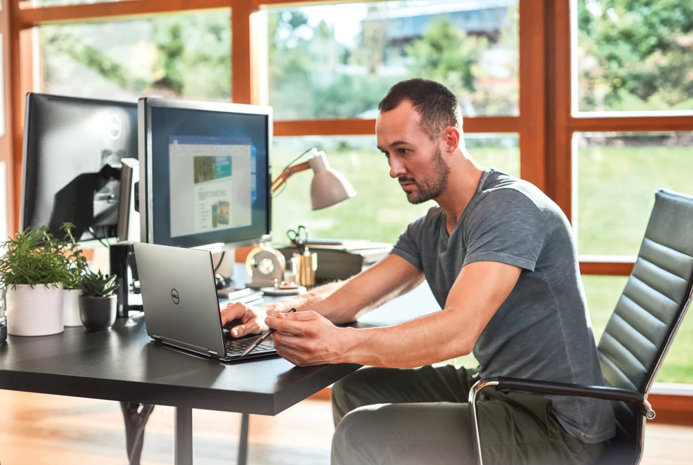 A man sitting at a laptop working by an open window.