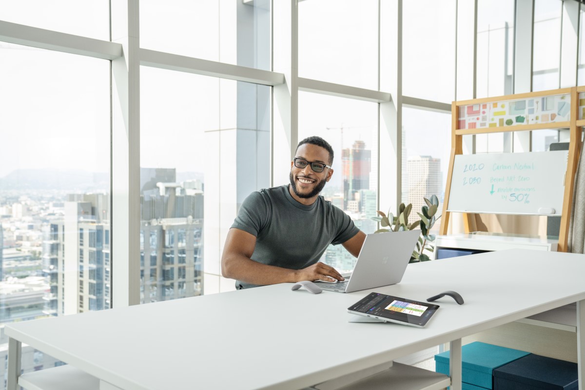 Person sitting at a desk with a laptop, smiling, looking to the side.
