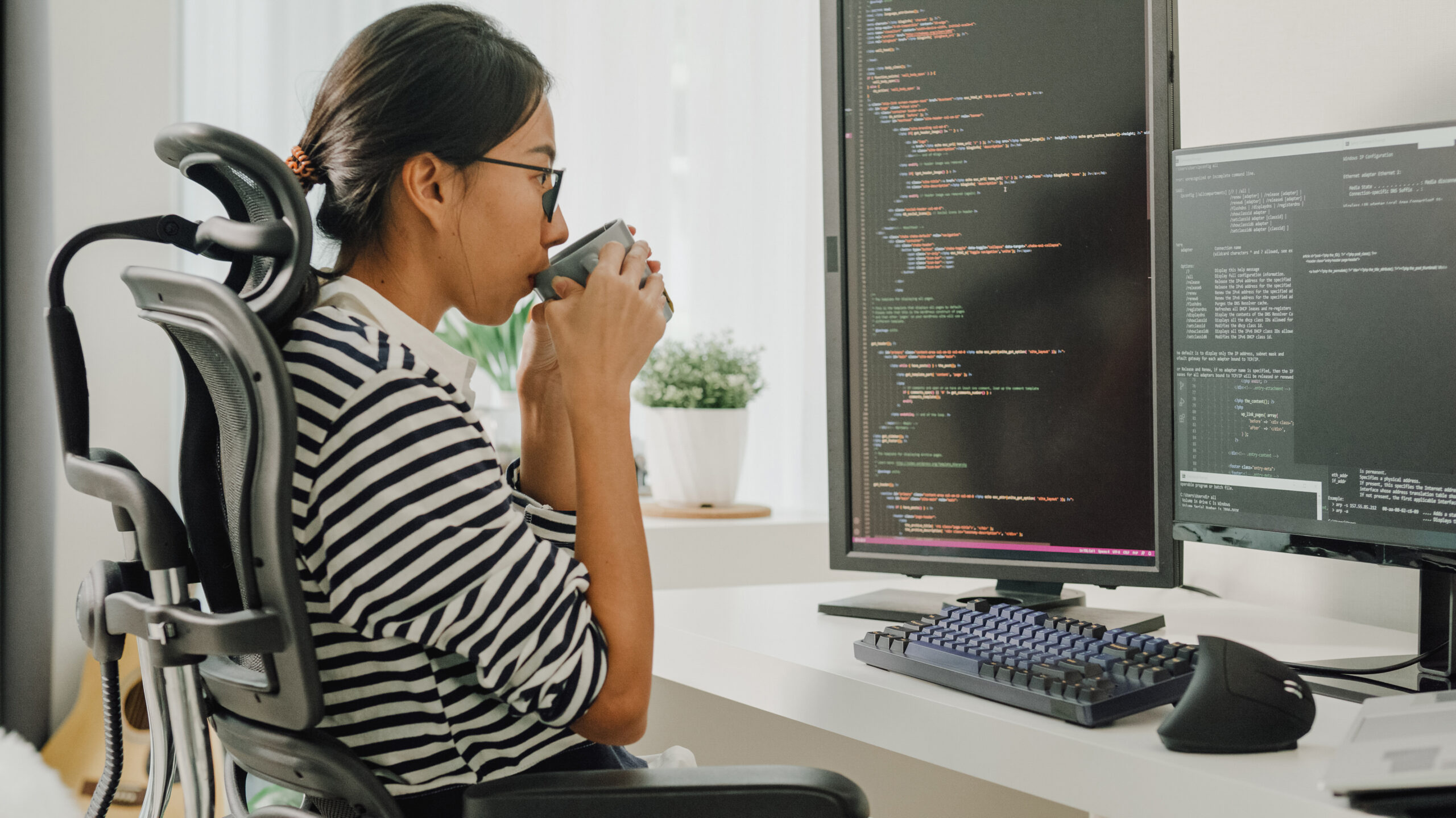 A woman drinking from a cup in front of a computer