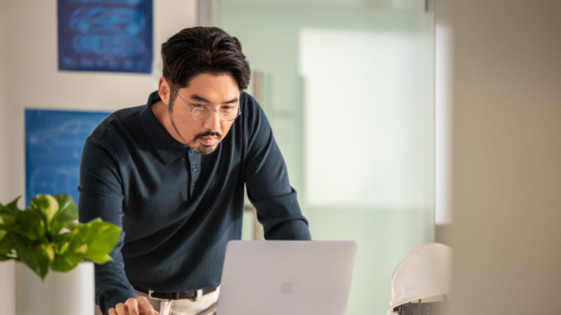 A man in a blue shirt and glasses looking at a laptop