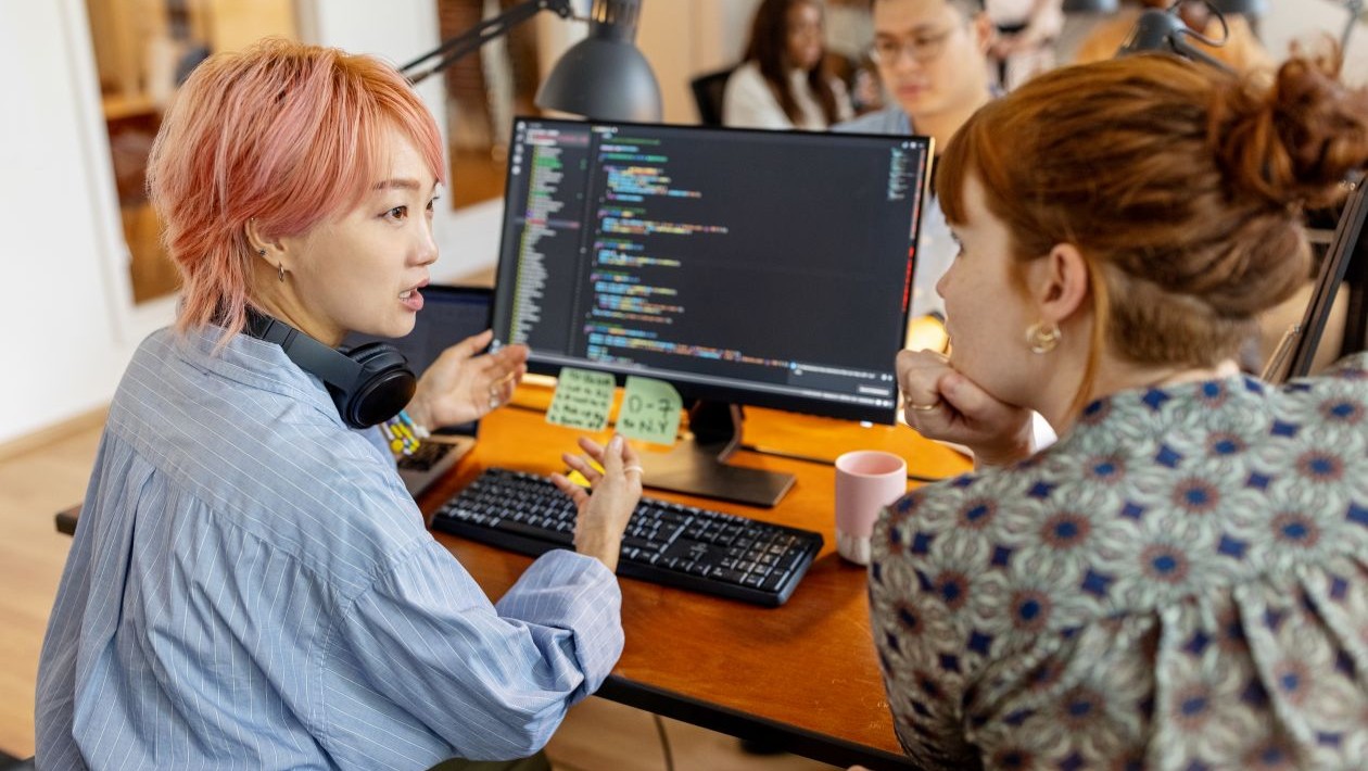 A group of people sitting at a desk looking at a computer screen