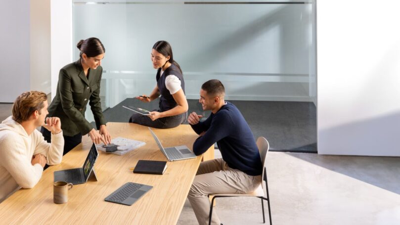 A group of people sitting around a table with laptops