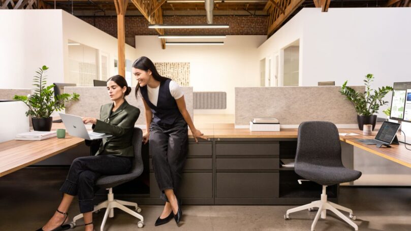 Two coworkers working in cubicle looking at computer monitor.