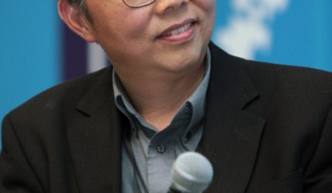 Stan Shih wearing a suit and tie holding a glass of wine