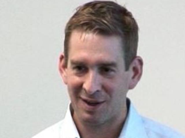 a man wearing a suit and tie smiling at the camera