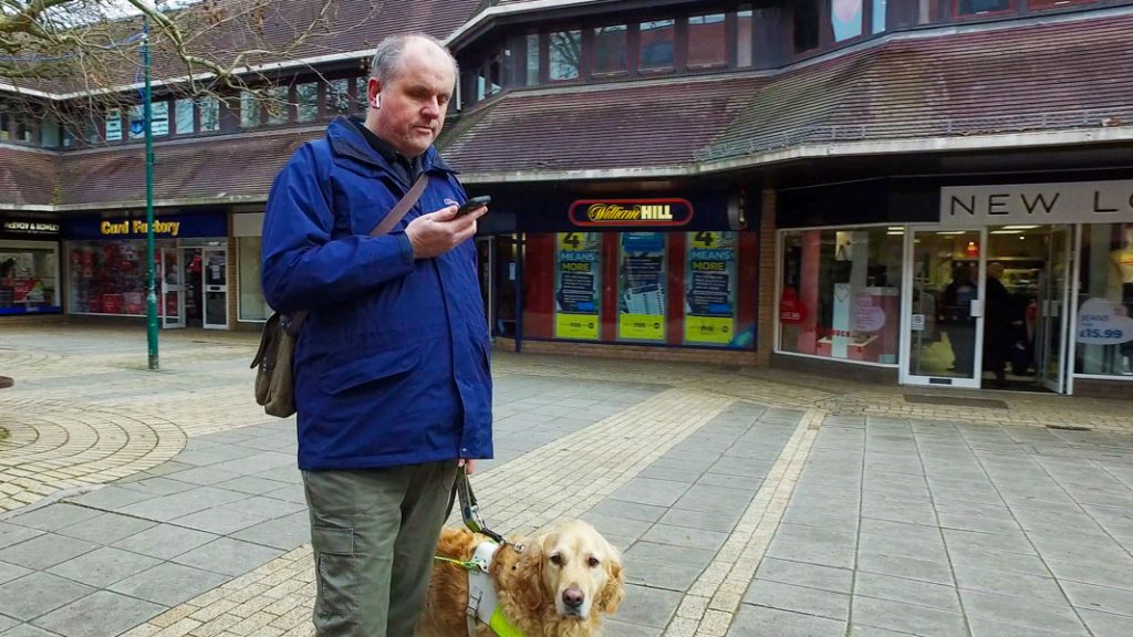 Man holding a smart phone, standing next to his guide dog