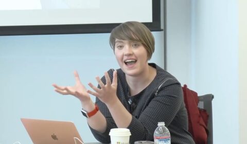 a woman sitting at a table with a laptop and smiling at the camera