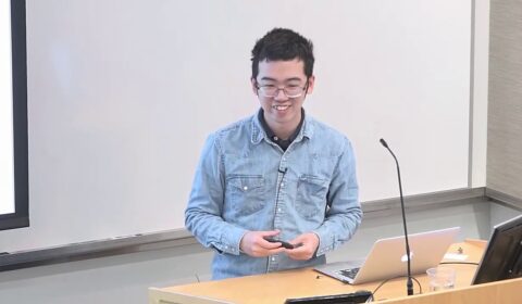 a person sitting at a table with a laptop and smiling at the camera