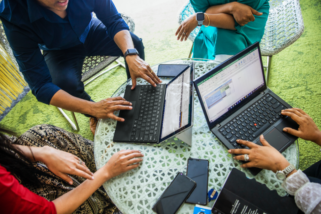 four people working together at a round table on two laptops