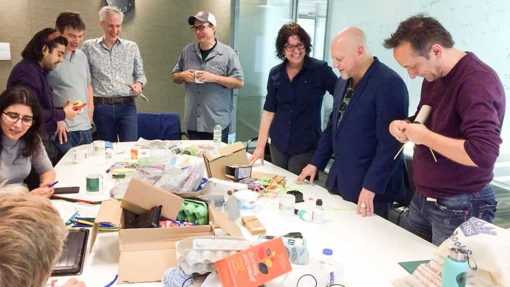 a group of people standing around a table working on a spreadsheet exercise