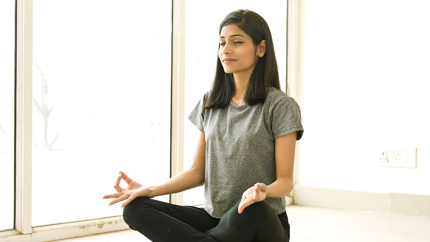 a woman meditating sitting with her eyes closed in a sunlit room
