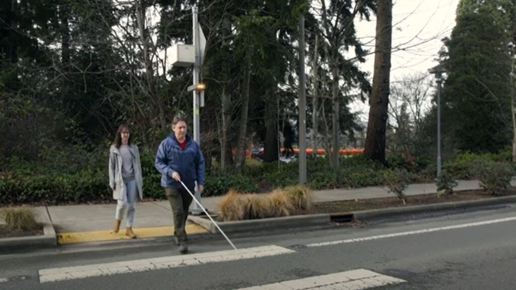 man using a cane on a crosswalk guided by Soundscape route audio beacons