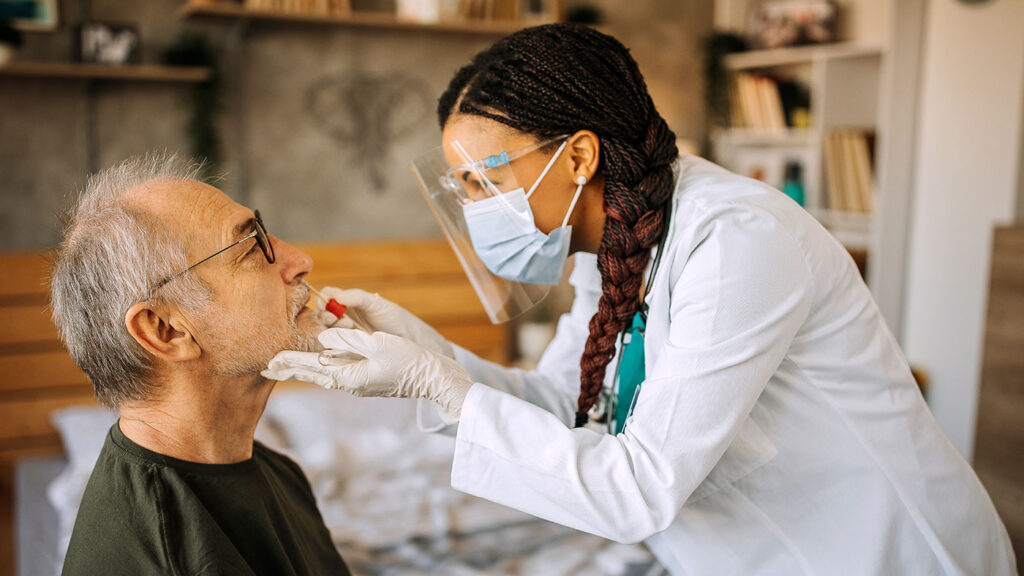 woman wearing a surgical mask swabbing the inside of an elderly man's nose