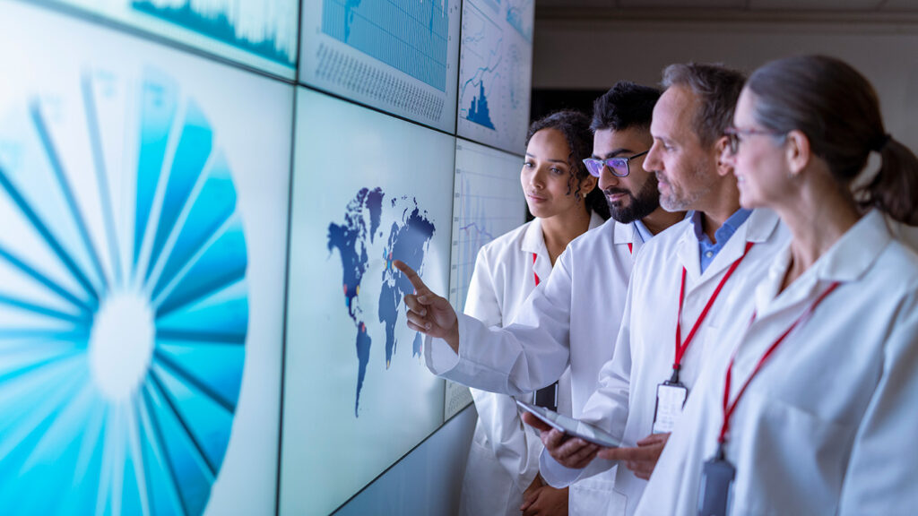 AI for Health - four people in lab coats conferring at a large monitor