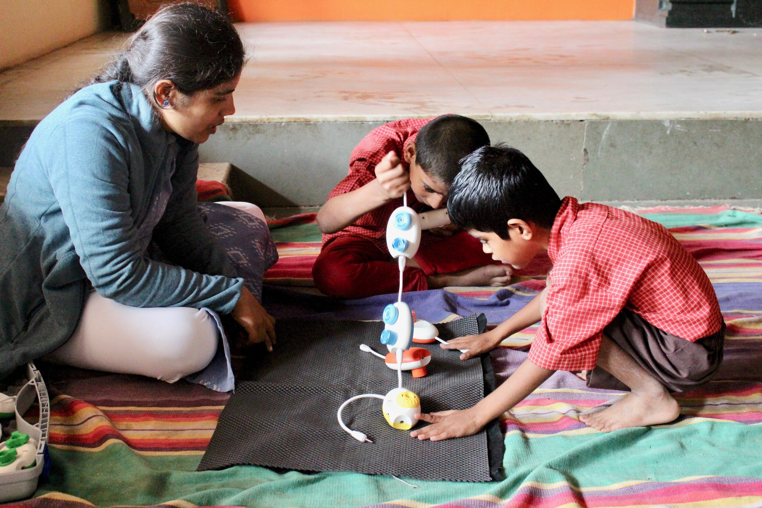 Two children sitting on the floor playing with CodeJumper while a facilitator looks on