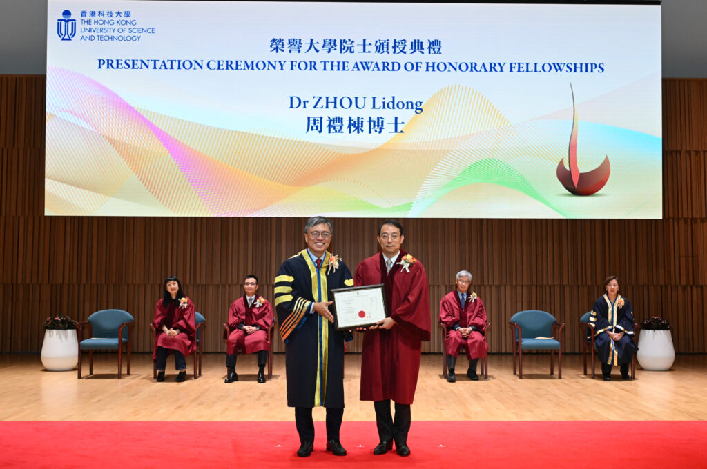 A presentation ceremony at The Hong Kong University of Science and Technology for the award of honorary fellowships. Lidong Zhou receives an award from HKUST Council Chairman Prof. Harry Shum on stage, both dressed in academic regalia. A large screen above displays the event title and Lidong’s name in English and Chinese, with colorful abstract graphics.