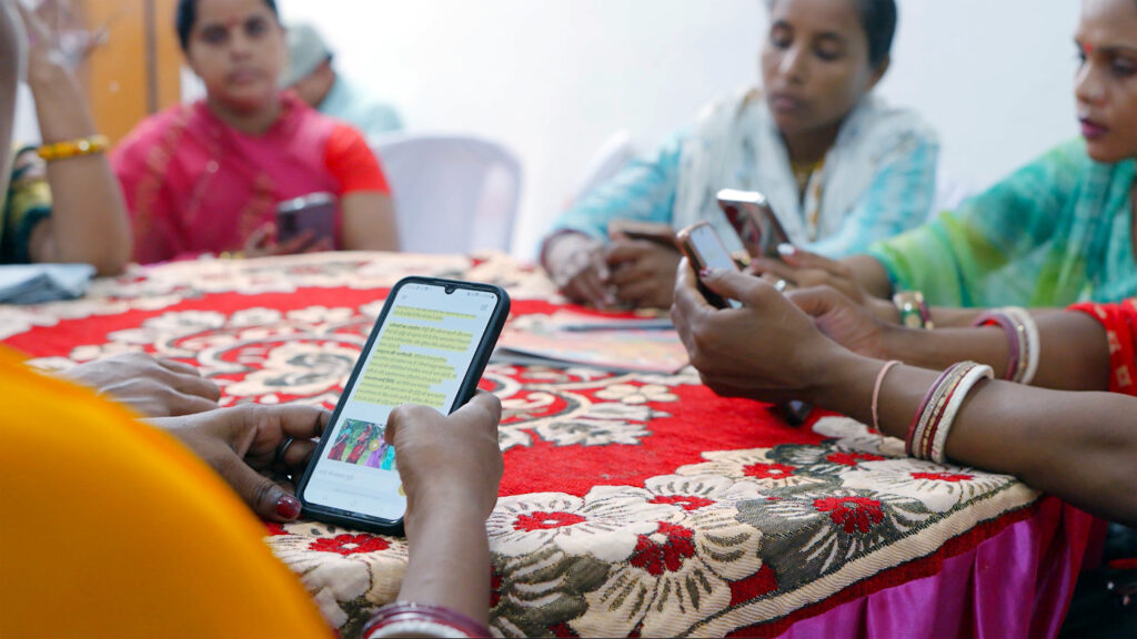 Farmers sitting around a table holding cellphones receiving step-by-step guidance on their farming questions.
