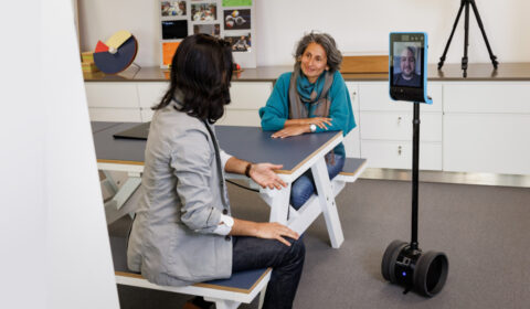 Collab AI group header | two people conversing with another person displayed on a virtual mobile device