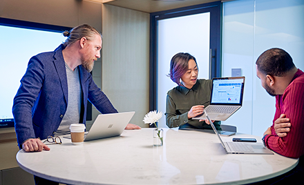 Image of three coworkers gathered around a laptop.