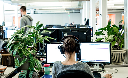 Image of a woman wearing headphones and looking at two computer monitors.