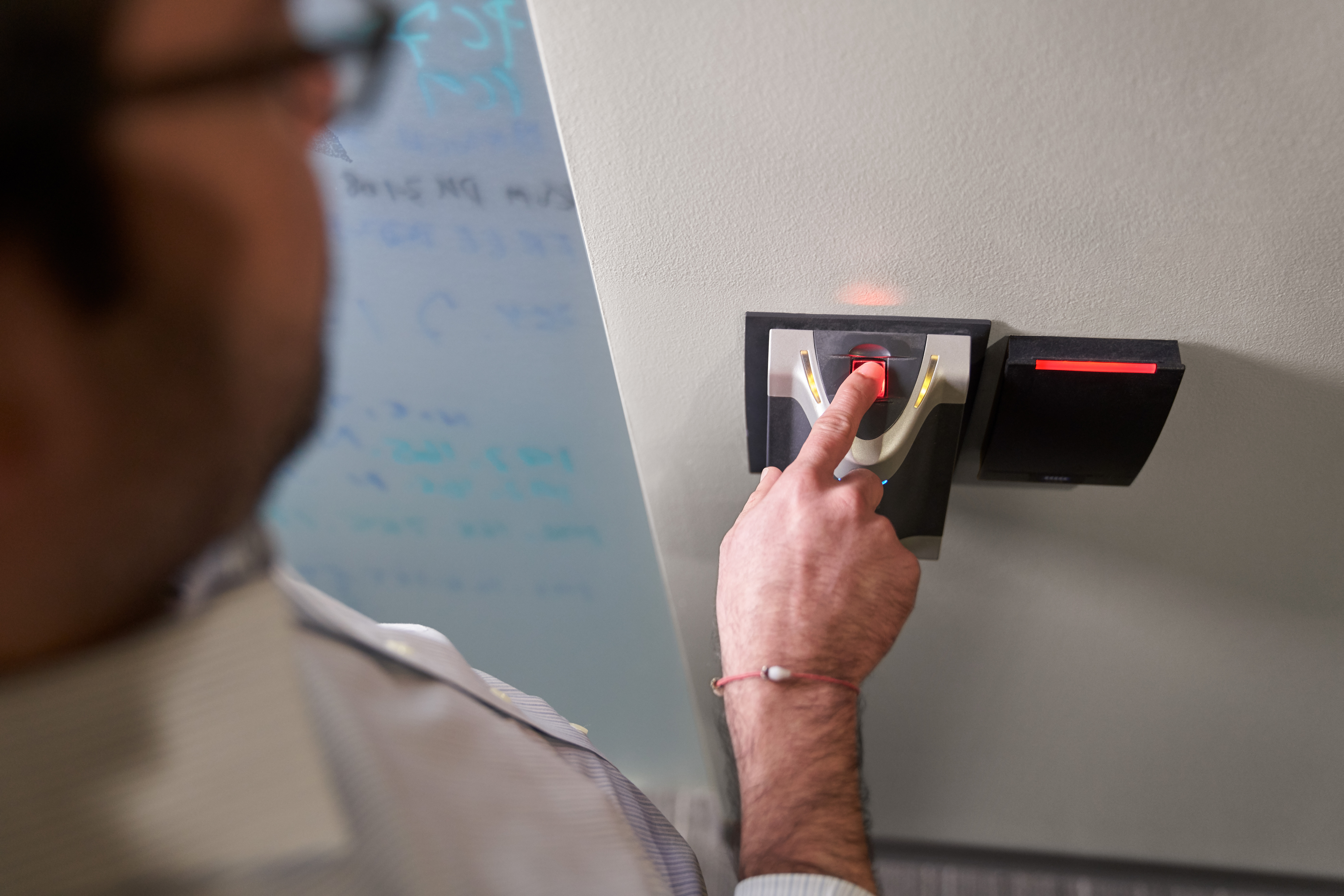 Man scanning his finger in a biometric fingerprint reader which will provide him access to a room.