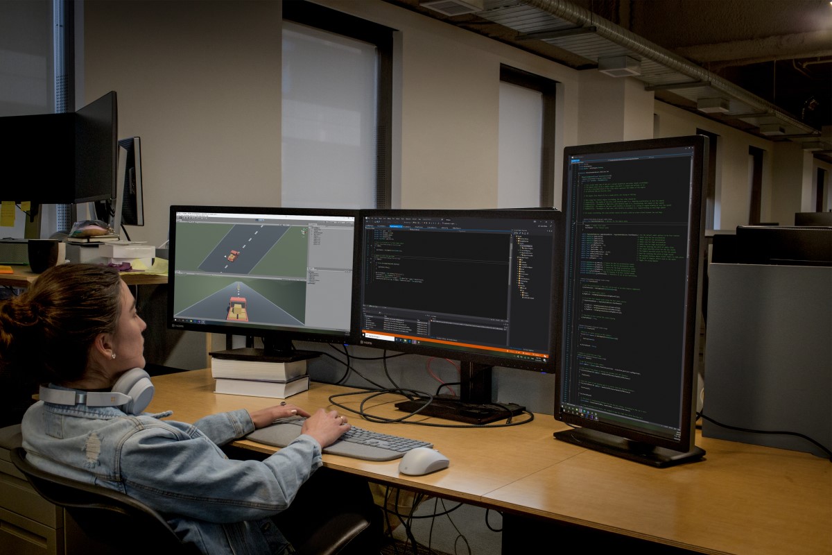 Real people, real offices. Female developer coding at her PC workspace in an enterprise office using Visual Studio on a multi-monitor set up.