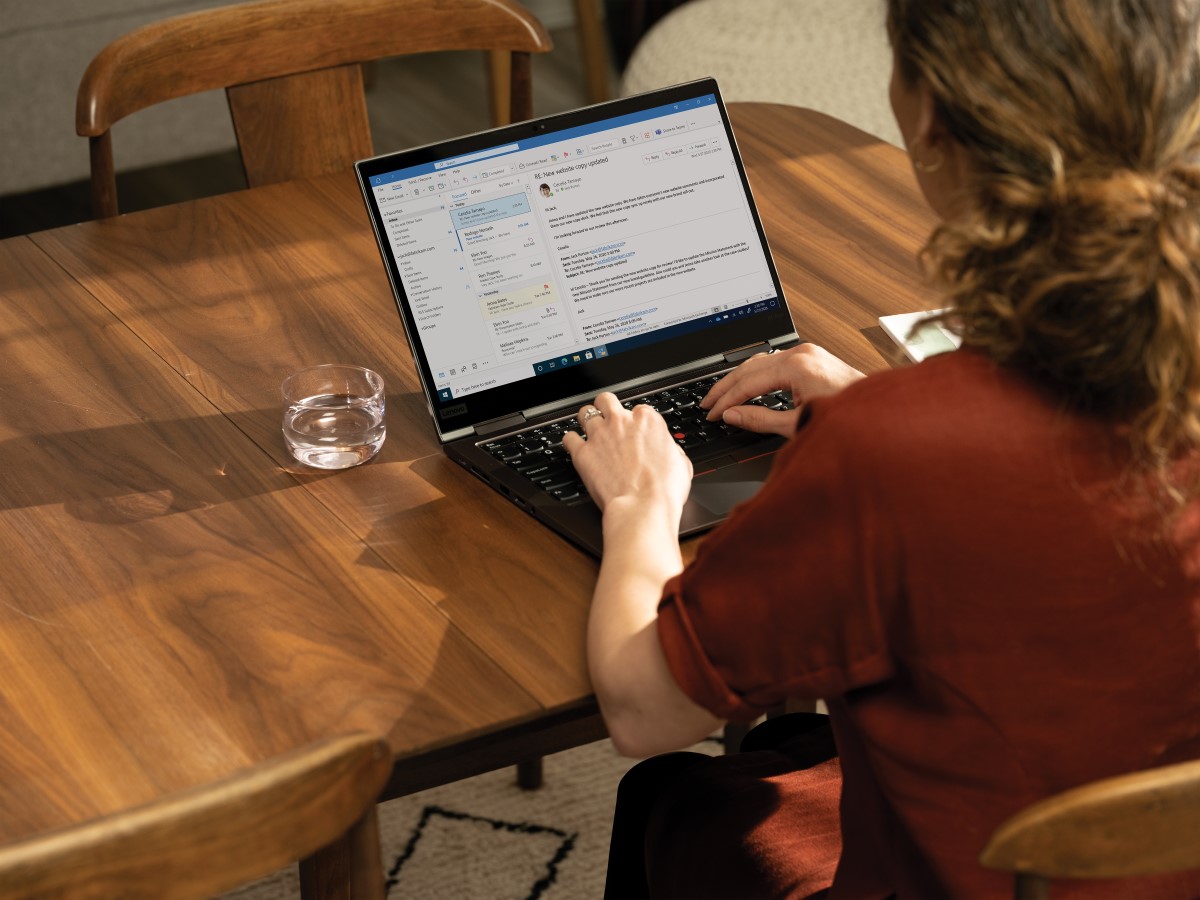 Over the shoulder photo of an adult woman at her dinning table looking at her Microsoft Outlook inbox.