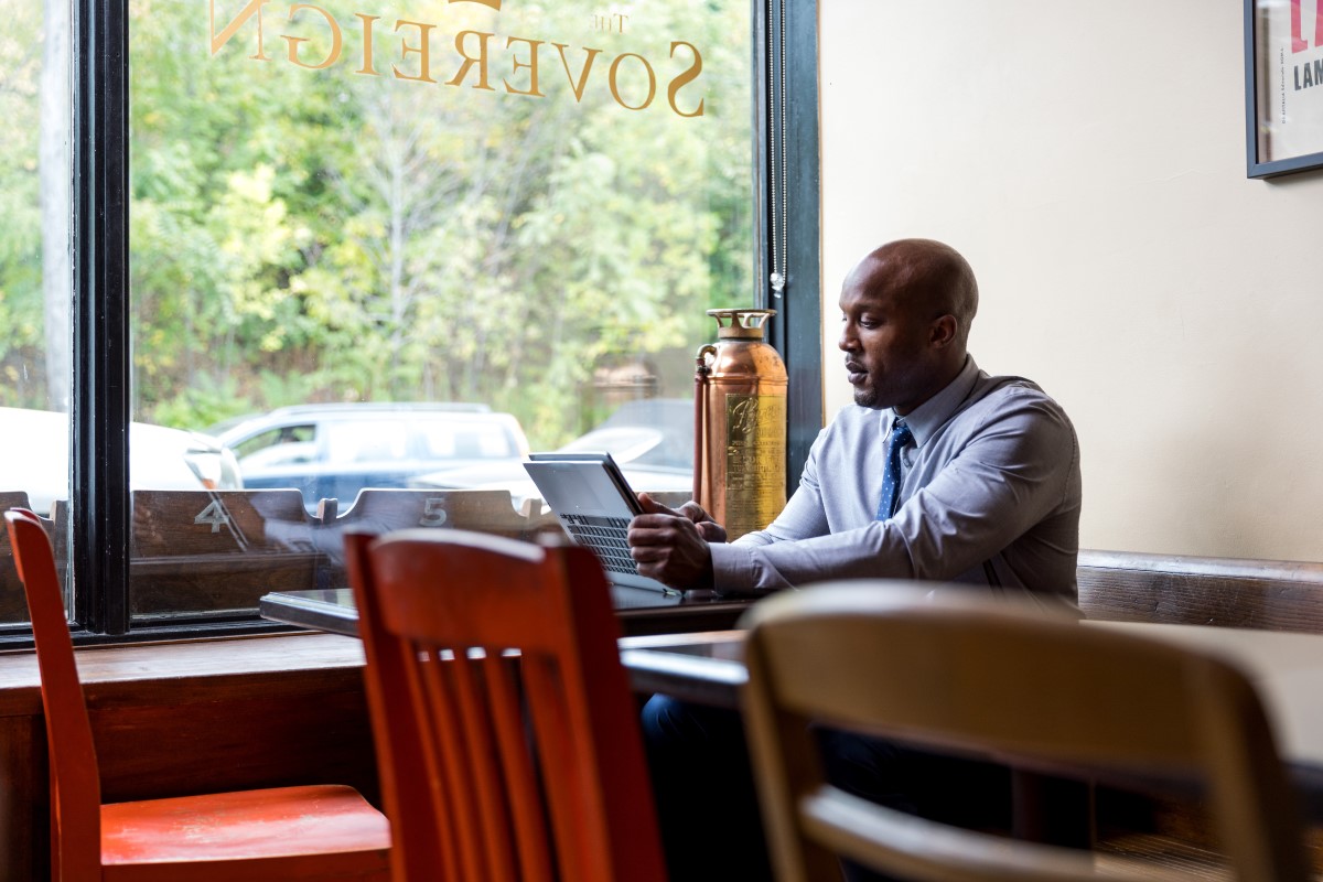 Male bank worker sitting in caf&eacute; restaurant using convertible laptop as tablet