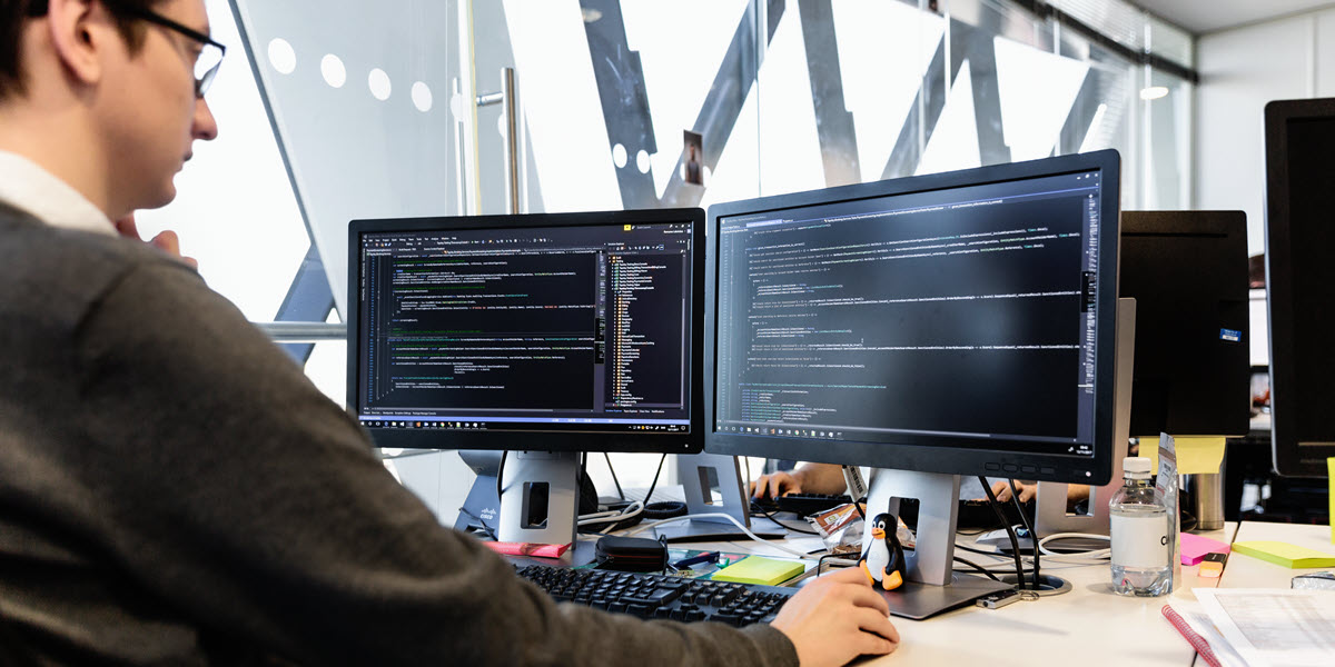 IT professional looking at computer screens that display lines of code.