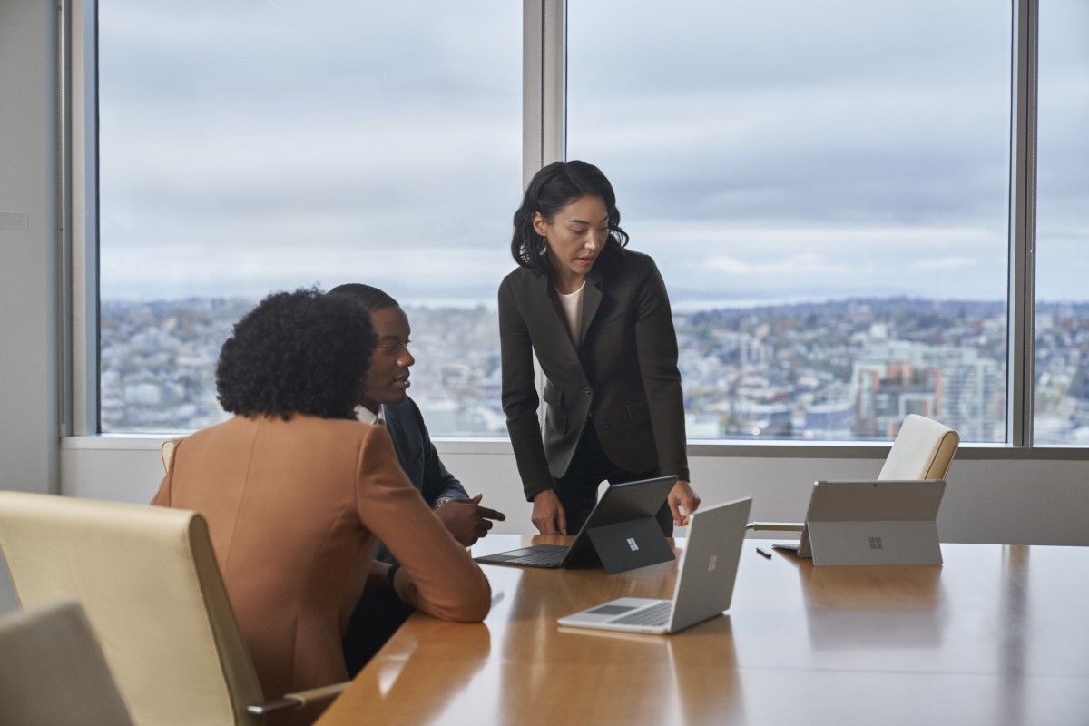 Conference room table with four people in a meeting with Surface Laptop Go 2 and Surface 2-in-1&lsquo;s.
