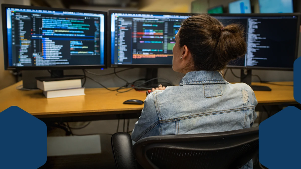 Photo of a developer coding her workspace in an enterprise office, using Visual Studio on a multi-monitor set up.