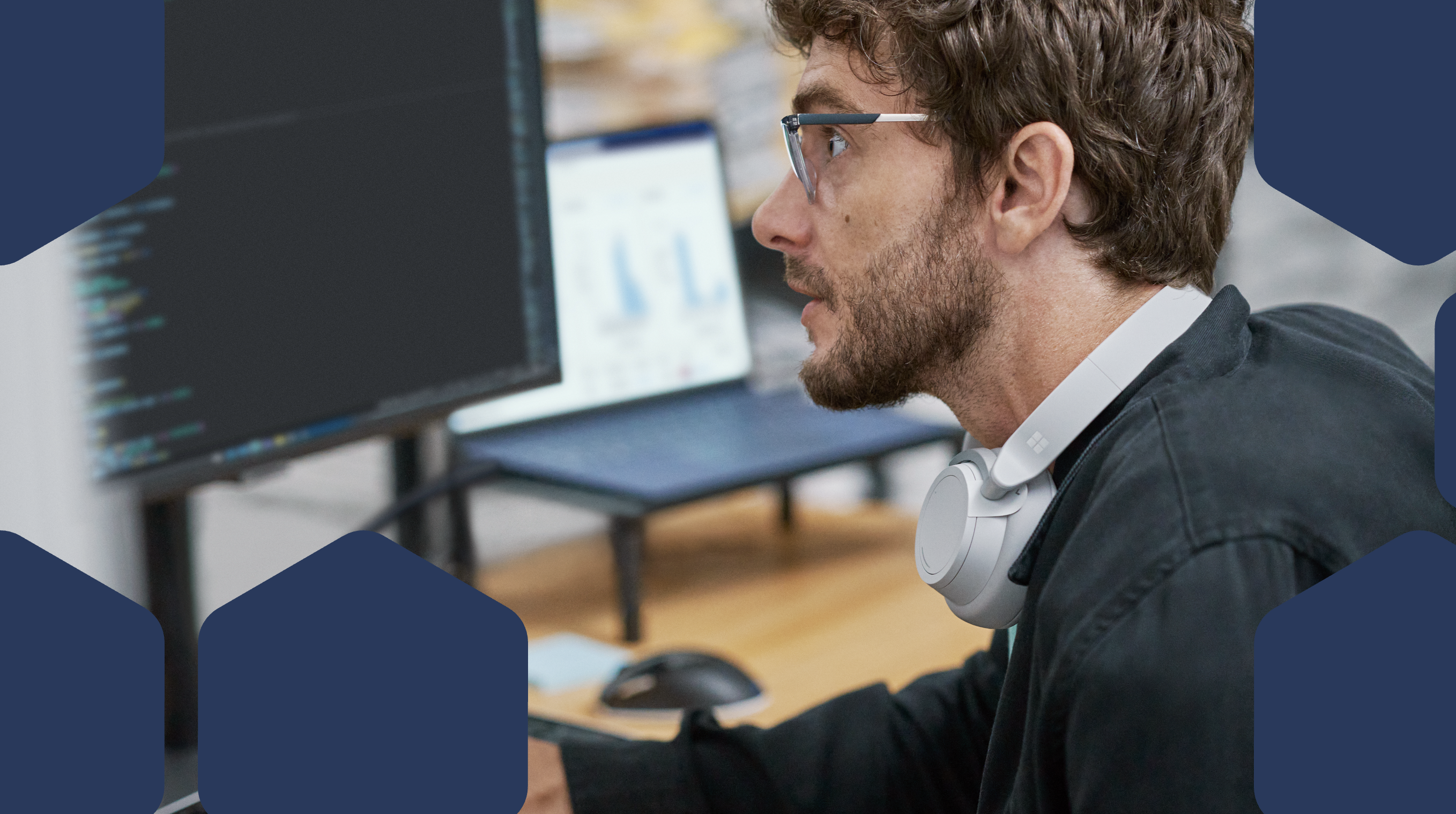 A man wearing glasses and headphones looking at a computer screen