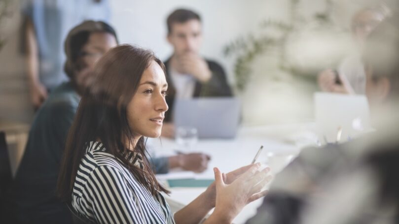 A woman sitting at a table with other people in the background