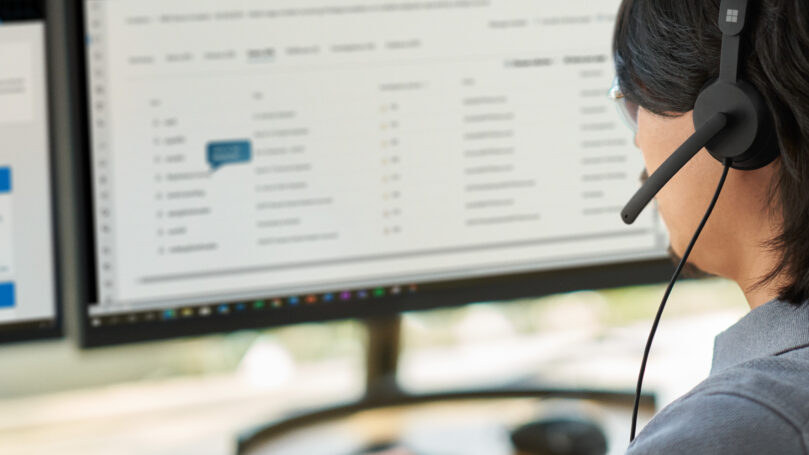 A woman wearing a headset and looking at a computer screen