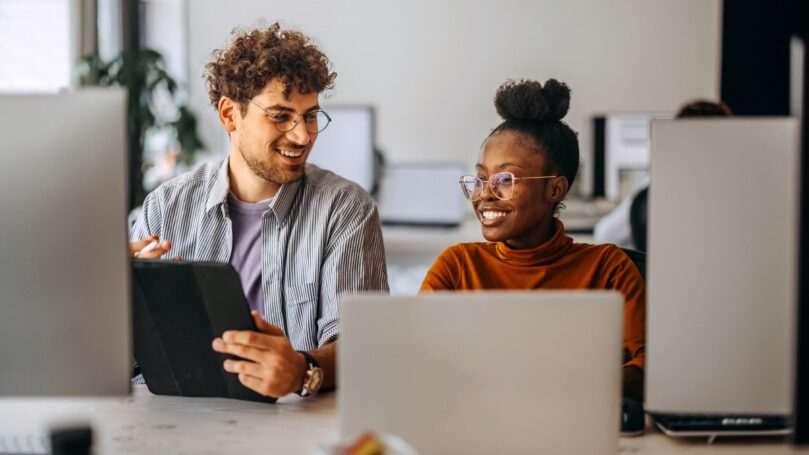 Two people sit behind computers.